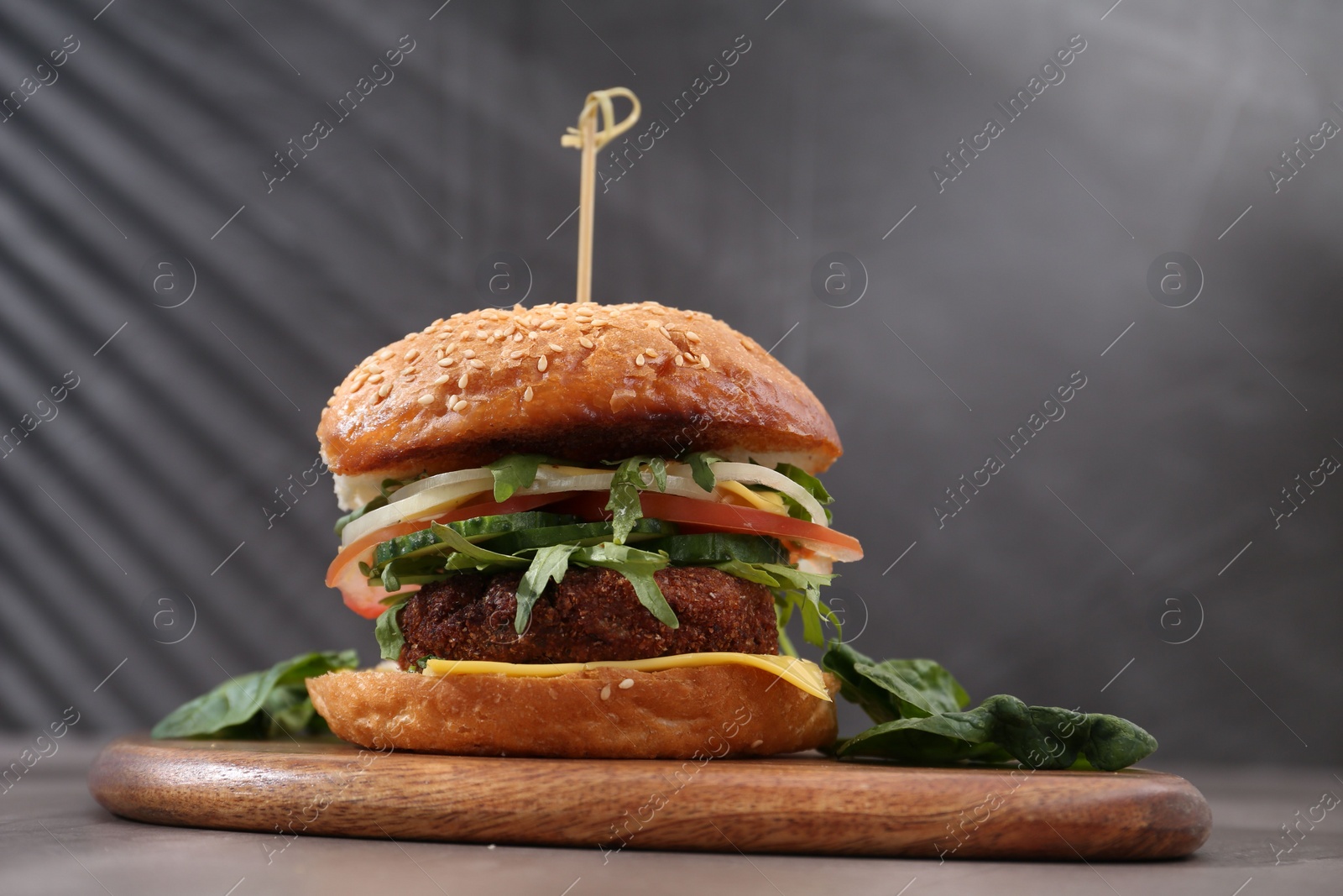 Photo of Board with delicious vegetarian burger on grey table