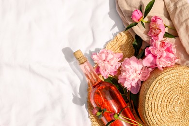 Flat lay composition with beautiful peonies and rose wine on white fabric, space for text