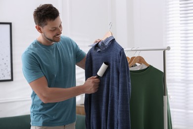 Photo of Man cleaning clothes with lint roller indoors