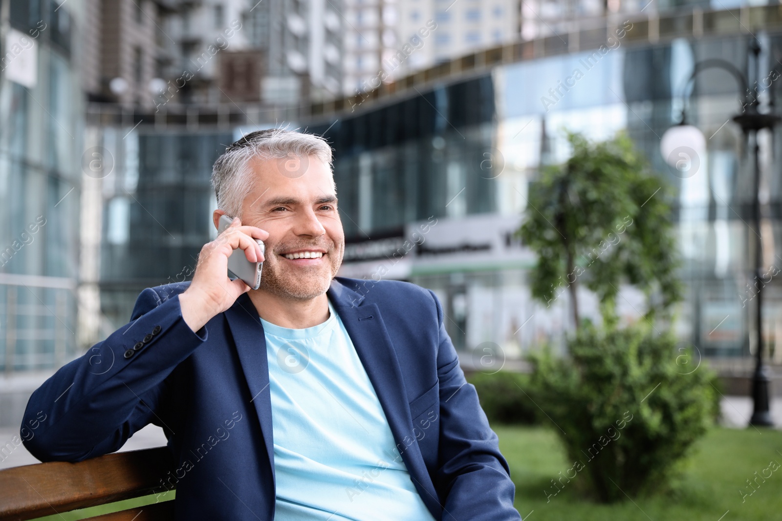 Photo of Portrait of handsome mature man talking on phone in city center. Space for text