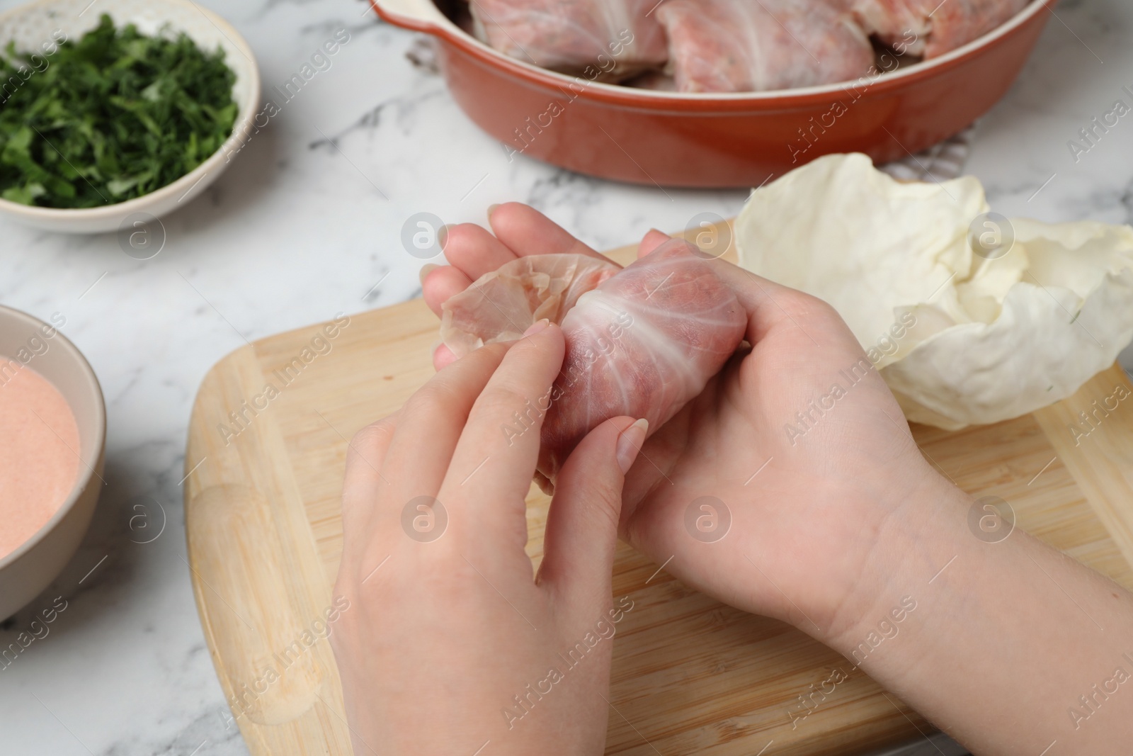 Photo of Woman making stuffed cabbage roll at white table, closeup