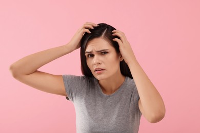Emotional woman examining her hair and scalp on pink background