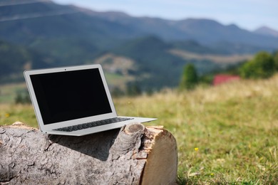 Laptop on wooden log in mountains, space for text. Distance work