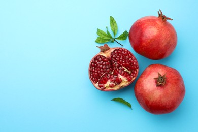 Photo of Fresh pomegranates and green leaves on light blue background, flat lay. Space for text