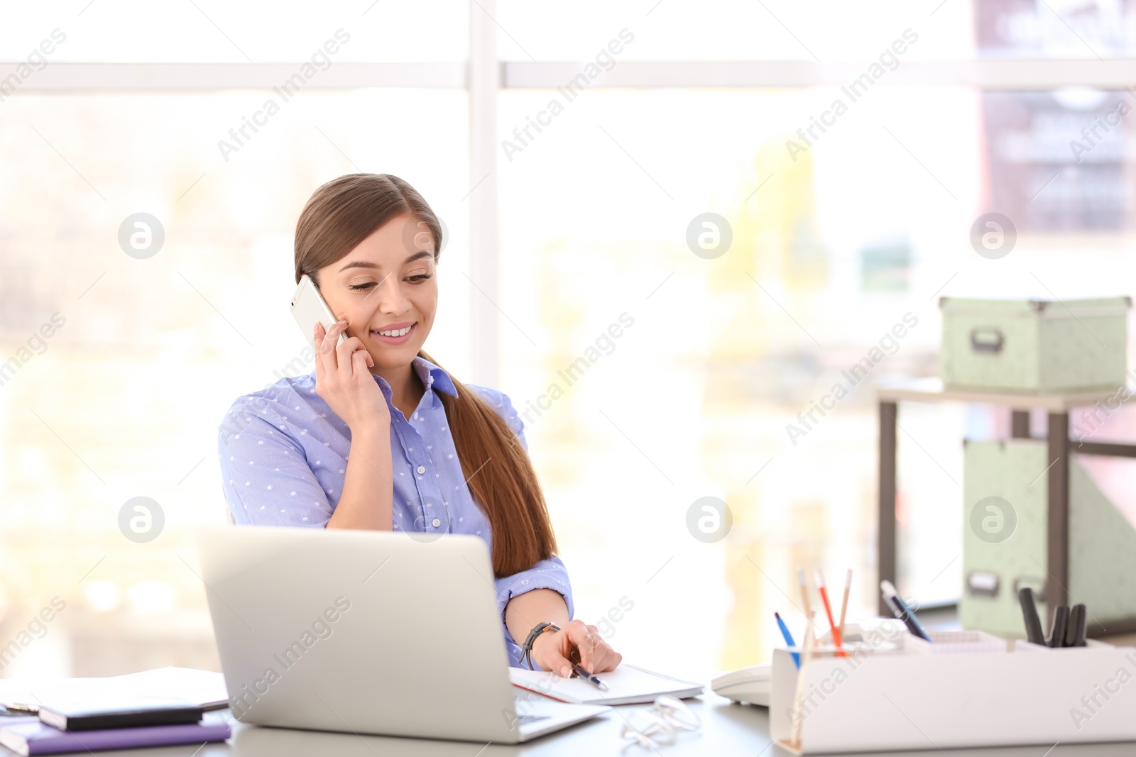 Photo of Young woman talking on phone at workplace