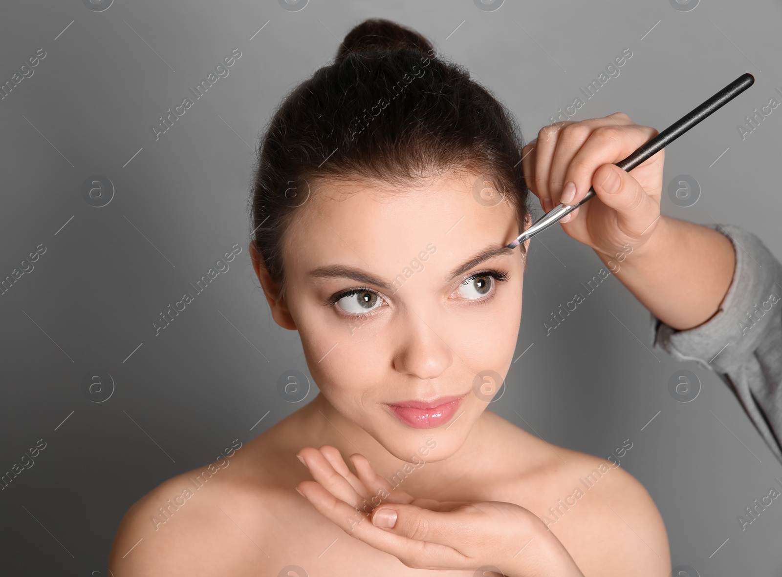 Photo of Visage artist applying makeup on woman's face against grey background. Professional cosmetic products