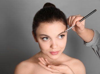 Photo of Visage artist applying makeup on woman's face against grey background. Professional cosmetic products