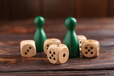 Many dices and green game pieces on wooden table, closeup