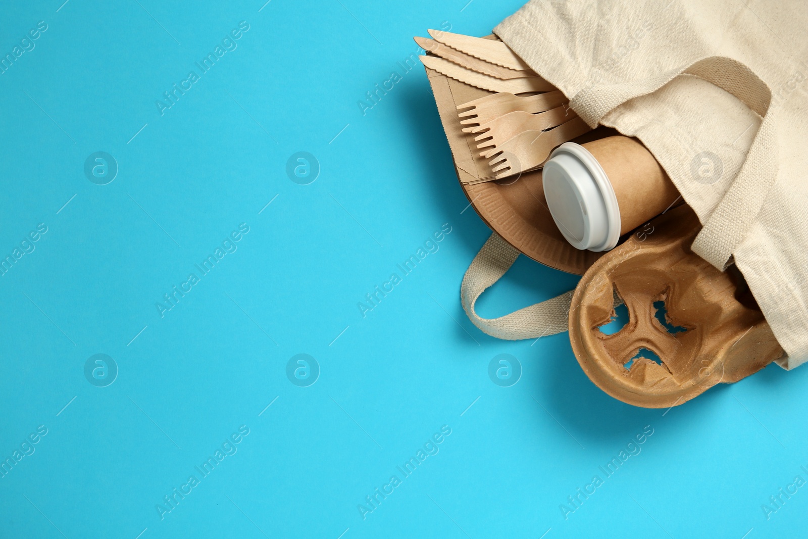 Photo of Flat lay of paper and wooden tableware in cotton bag on turquoise background, space for text. Eco friendly lifestyle