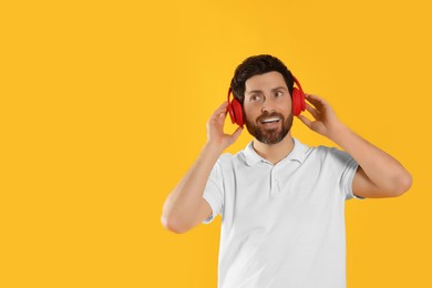 Photo of Happy man listening music with headphones on yellow background. Space for text