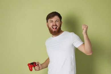 Emotional man with game controller on pale green background