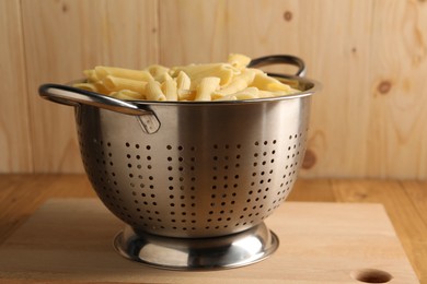 Cooked pasta in metal colander on wooden table, closeup