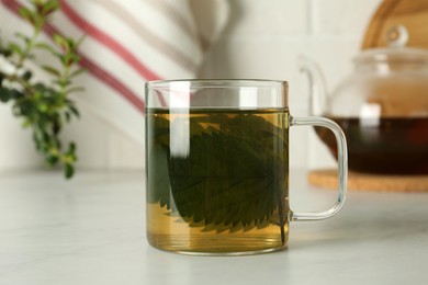 Photo of Glass cup of aromatic nettle tea on white table