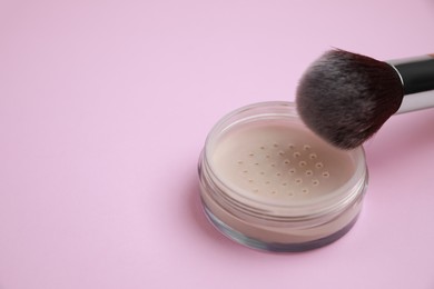 Photo of Loose face powder and brush on pink background, space for text