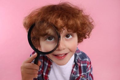Photo of Cute little boy looking through magnifier glass on pink background