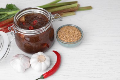 Photo of Tasty rhubarb sauce and ingredients on white wooden table, space for text