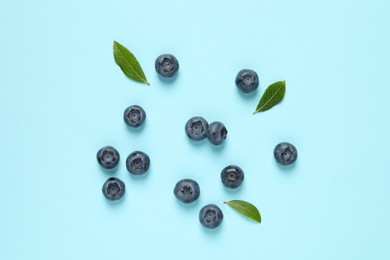 Photo of Tasty fresh blueberries with green leaves on light blue background, flat lay