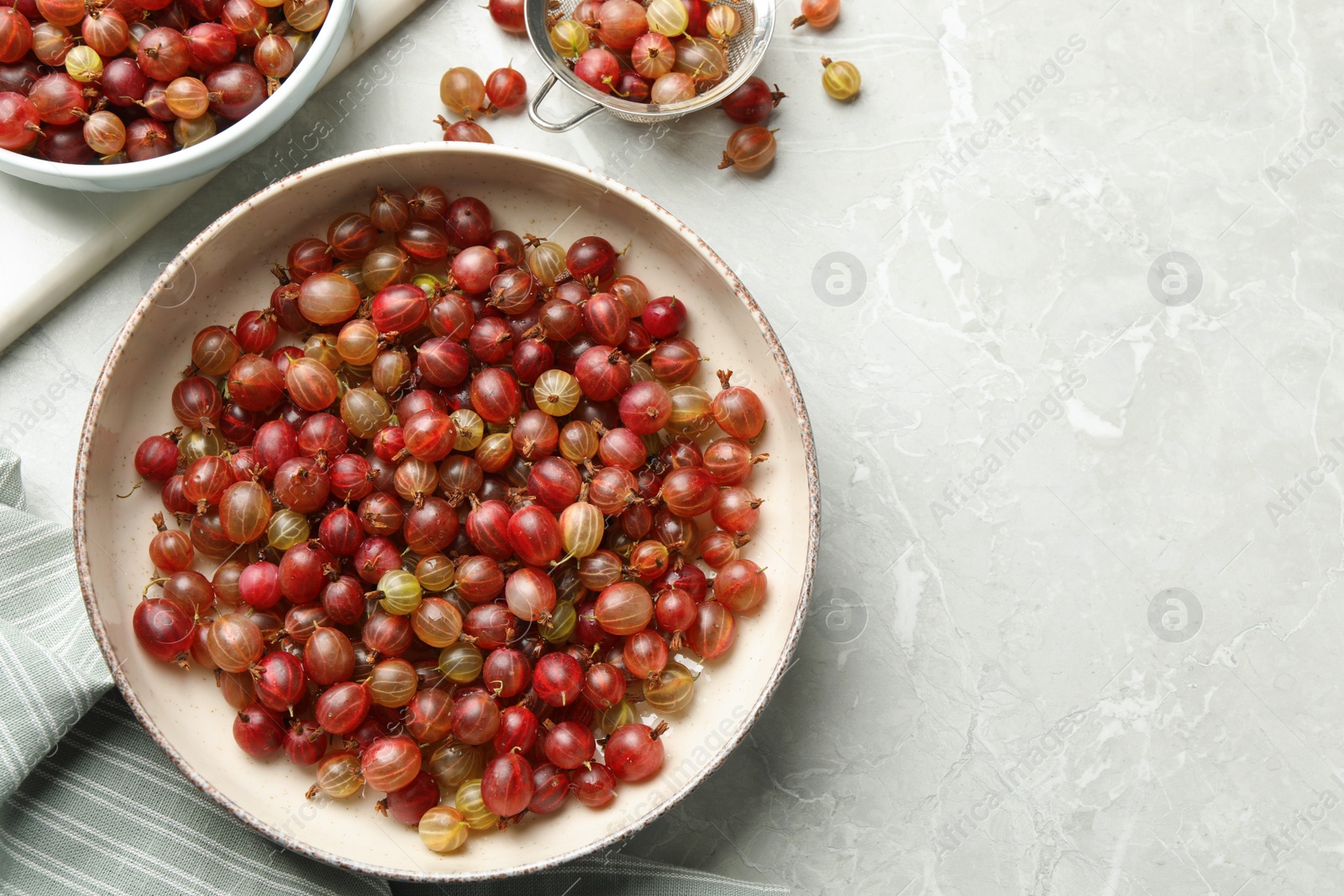 Photo of Ripe gooseberries on light grey marble table, flat lay. Space for text