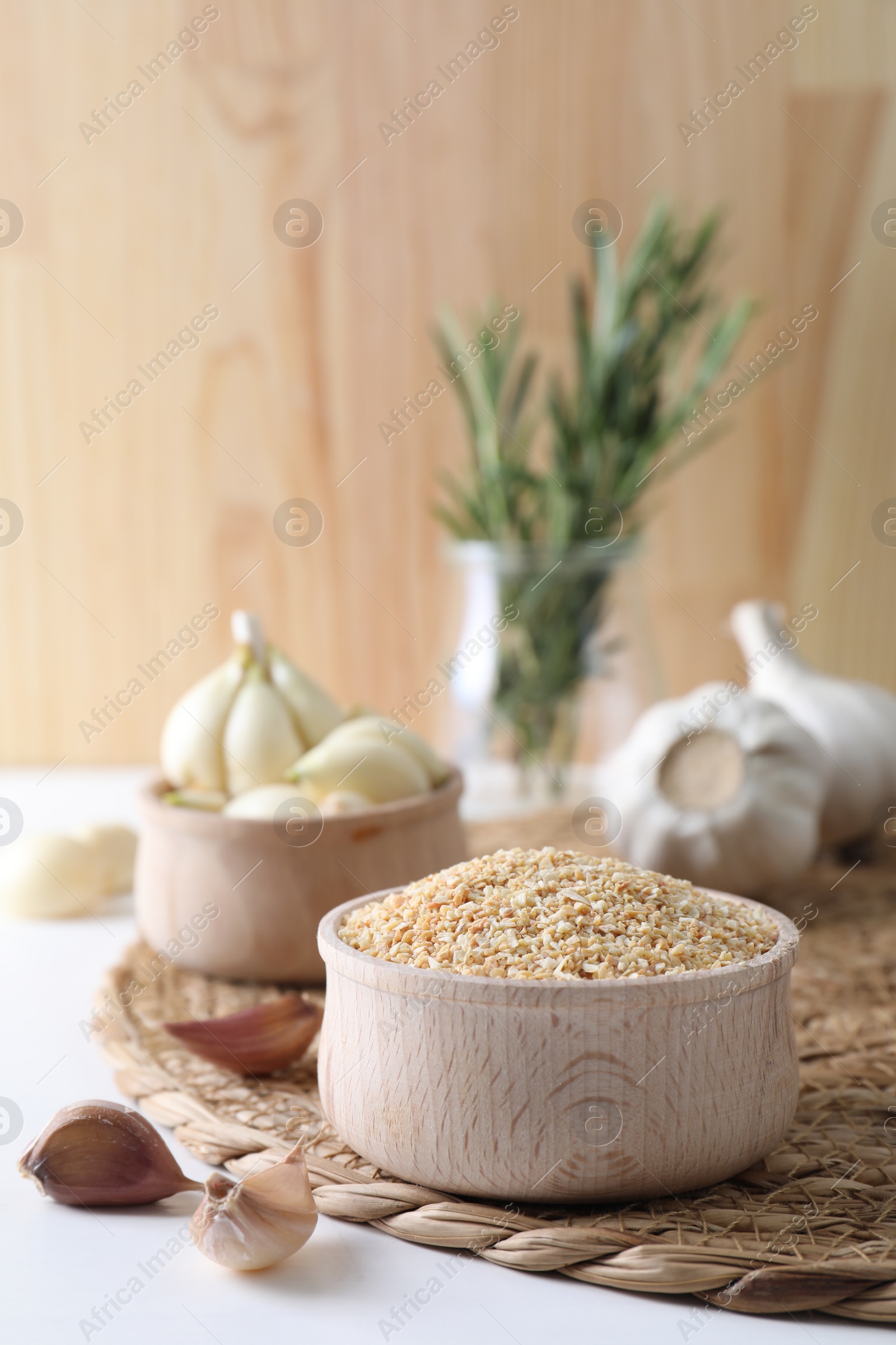 Photo of Dehydrated garlic granules in bowl, fresh bulbs and cloves on white table