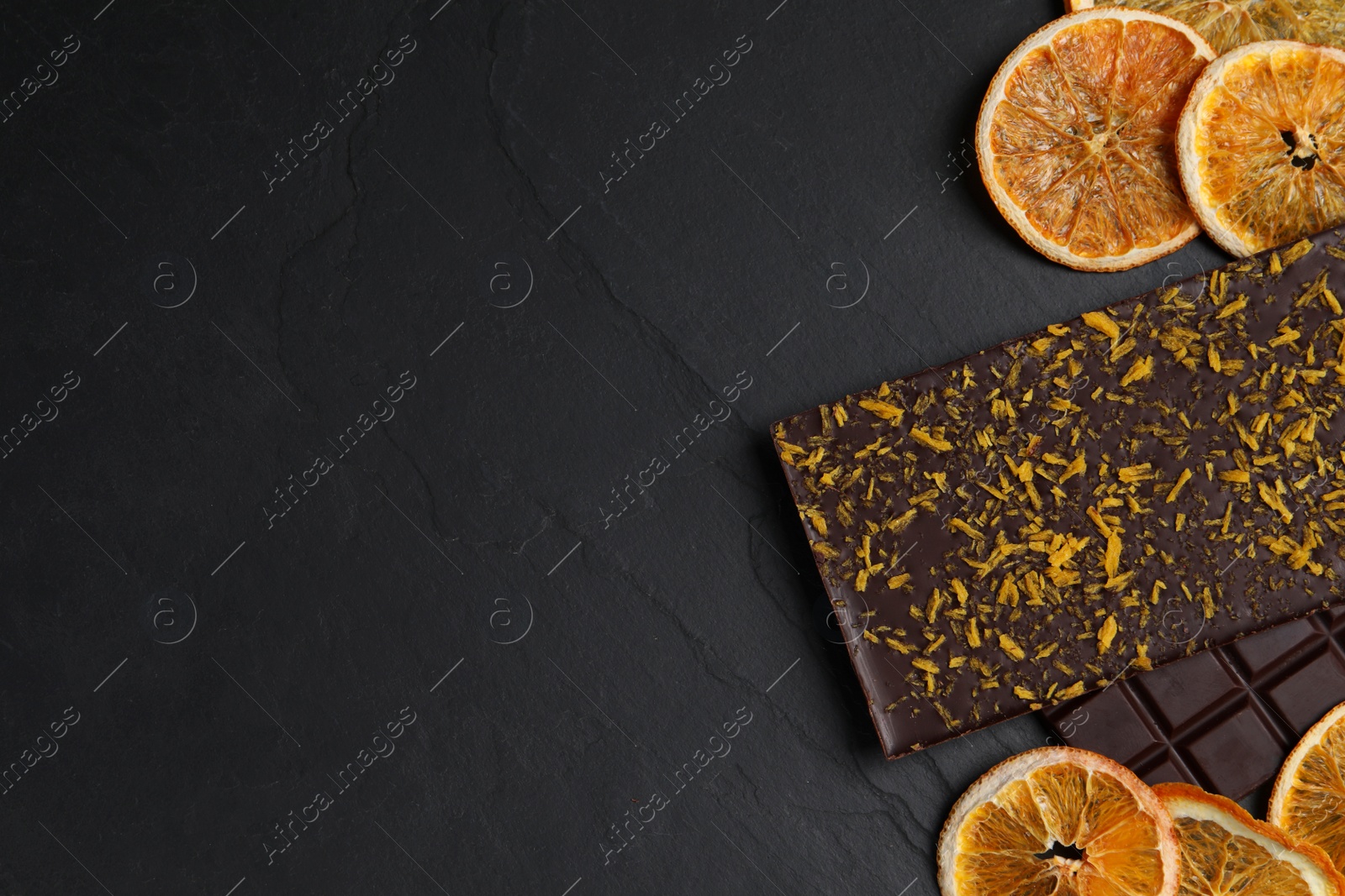 Photo of Chocolate bars with freeze dried orange on slate table, flat lay. Space for text