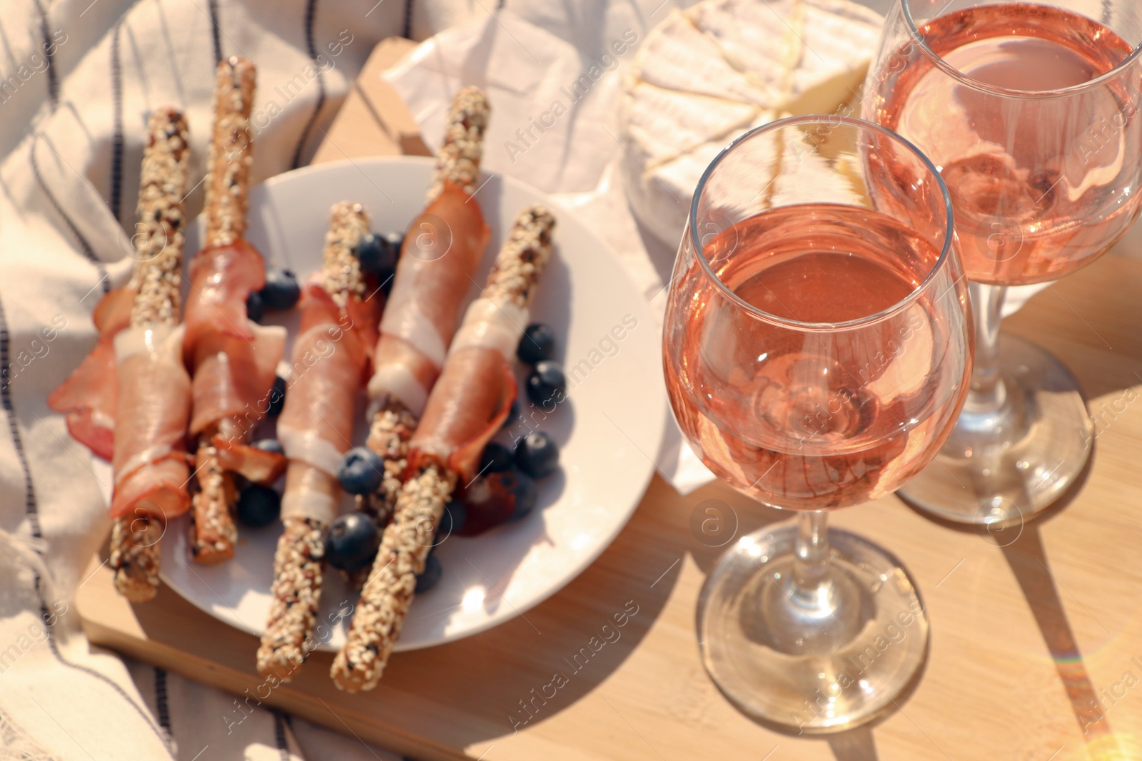 Photo of Glasses of delicious rose wine and food on white picnic blanket