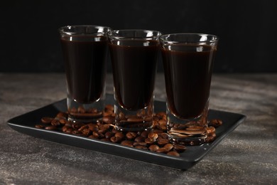 Shot glasses with coffee liqueur and beans on grey textured table