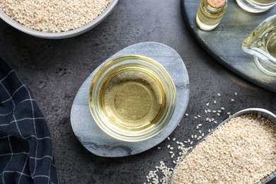 Sesame oil and seeds on dark grey table, flat lay