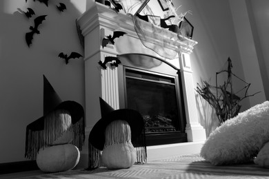 Photo of Beautiful black witch hats on pumpkins near fireplace indoors. Halloween celebration