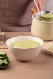 Photo of Woman with ladle pouring tasty leek soup at wooden table, focus on bowl