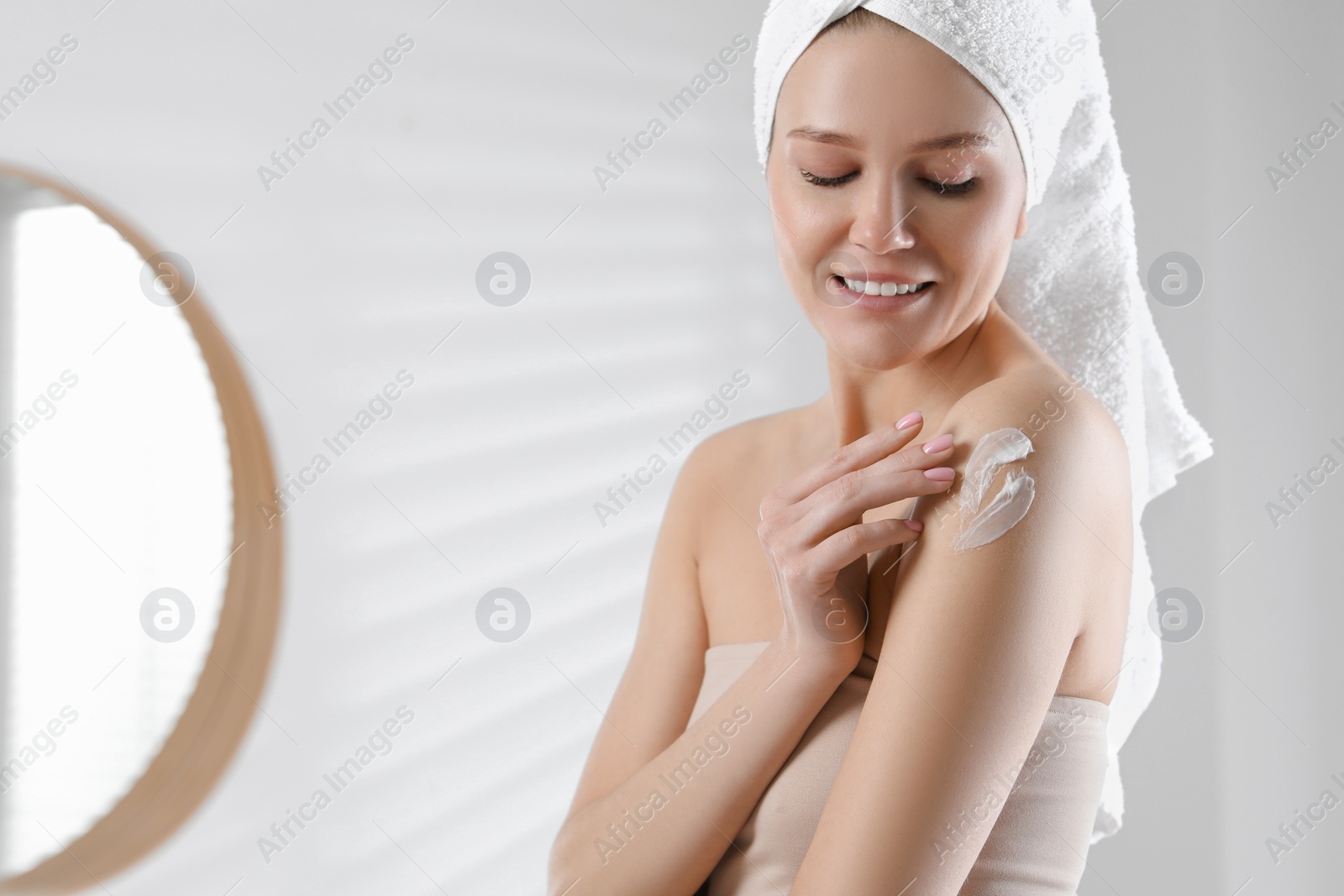 Photo of Happy woman applying body cream onto shoulder in bathroom, space for text