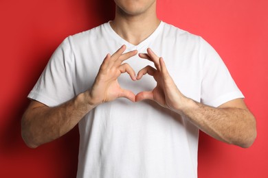 Photo of Man making heart with hands on red background, closeup