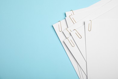 Photo of Sheets of paper with clips on light blue background, top view