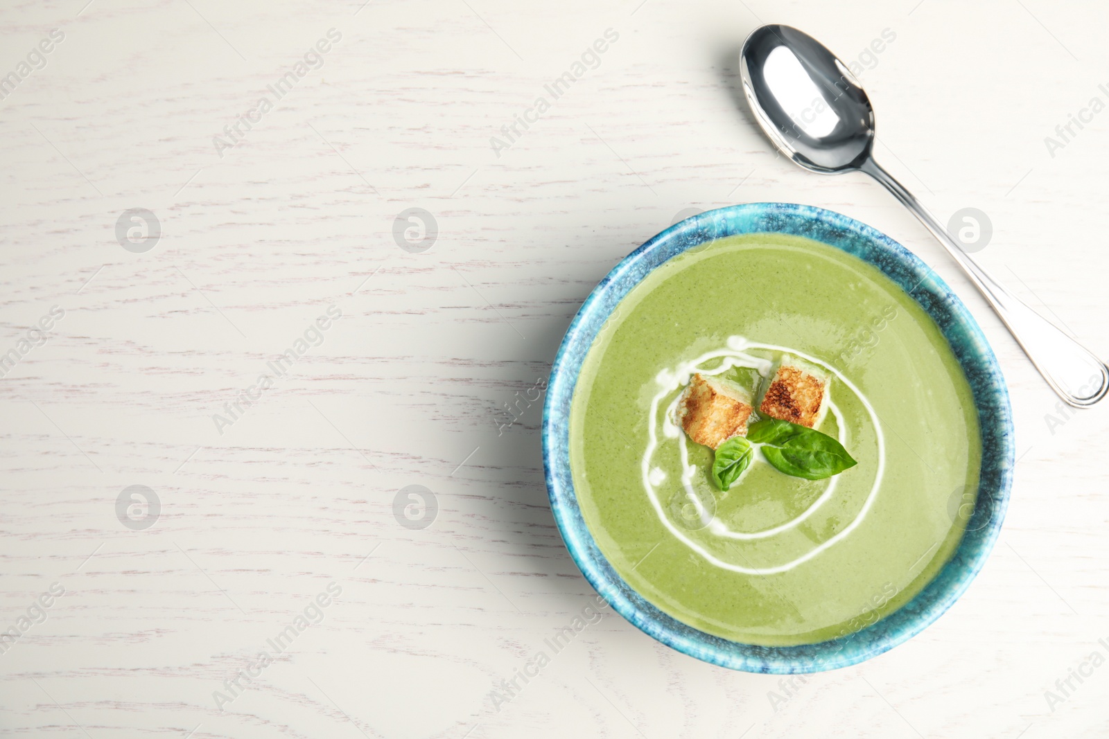 Photo of Delicious broccoli cream soup served on white wooden table, flat lay. Space for text