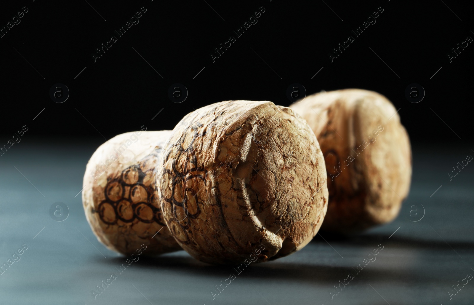 Photo of Corks of wine bottles with grape images on black table, closeup