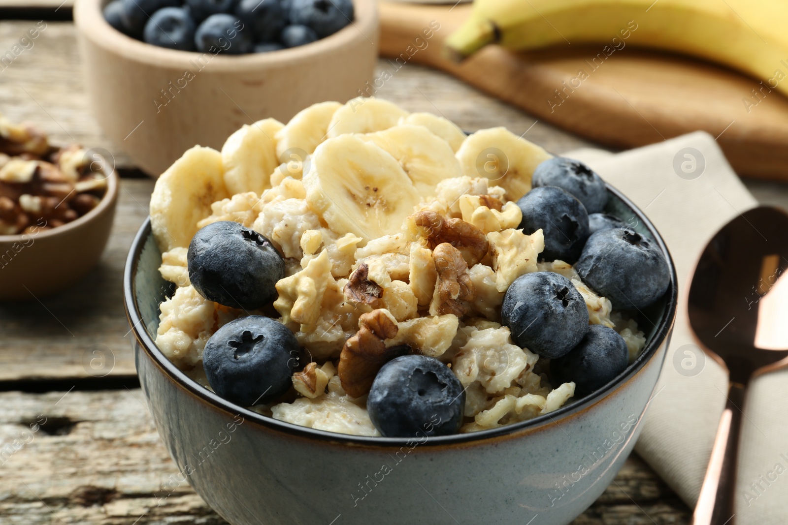 Photo of Tasty oatmeal with banana, blueberries and walnuts served in bowl on wooden table, closeup