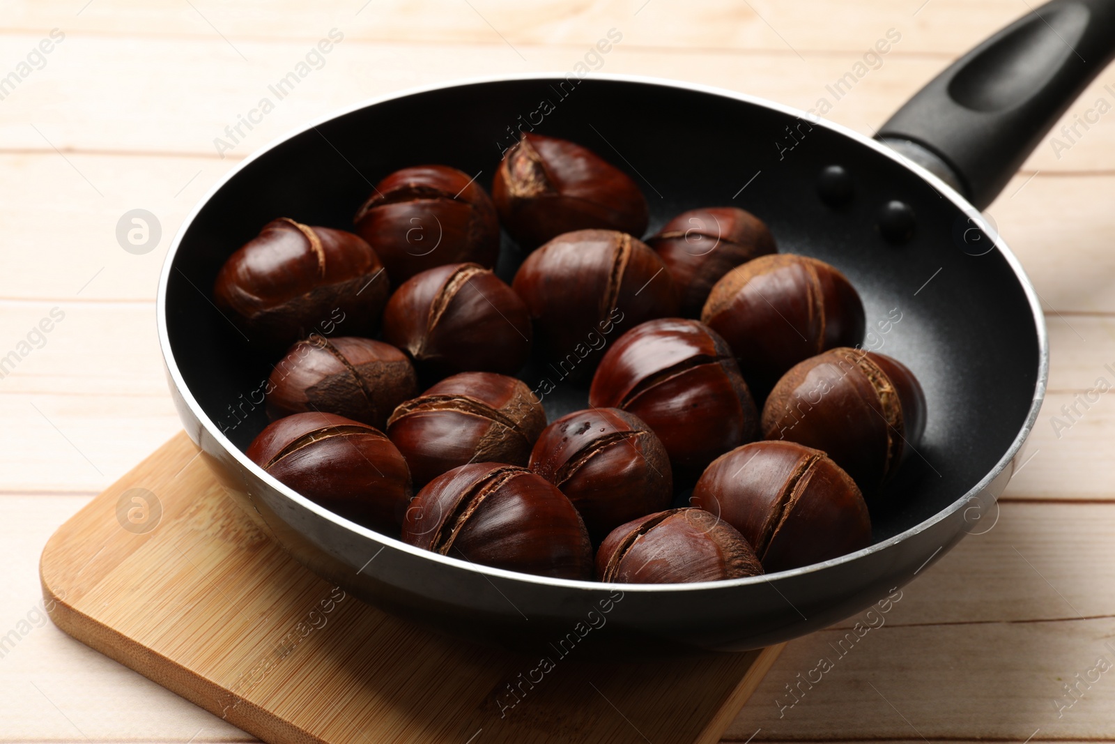 Photo of Roasted edible sweet chestnuts in frying pan on wooden table