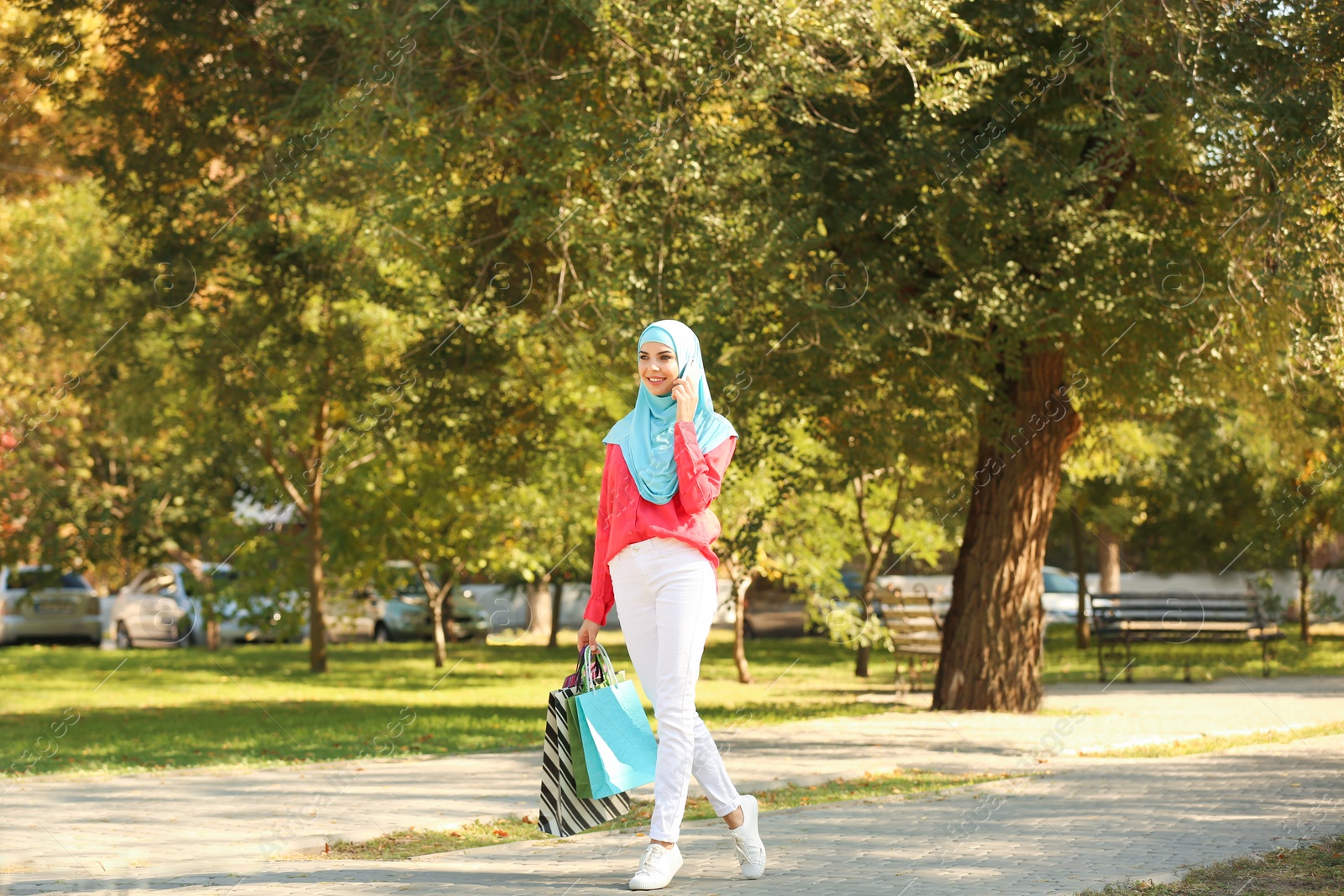 Photo of Muslim woman with shopping bags talking on phone in park