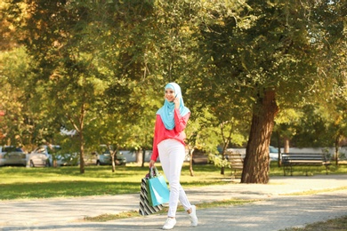Photo of Muslim woman with shopping bags talking on phone in park