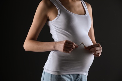 Photo of Young pregnant woman breaking cigarette on black background, closeup