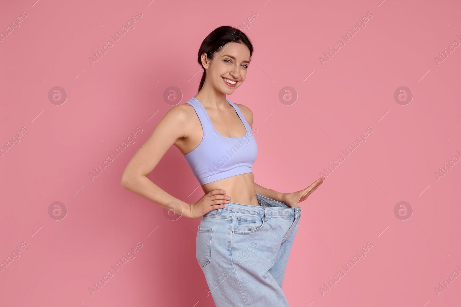 Photo of Happy young woman in big jeans showing her slim body on pink background