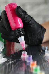 Tattoo artist dripping pink tattoo ink into cap on table, closeup