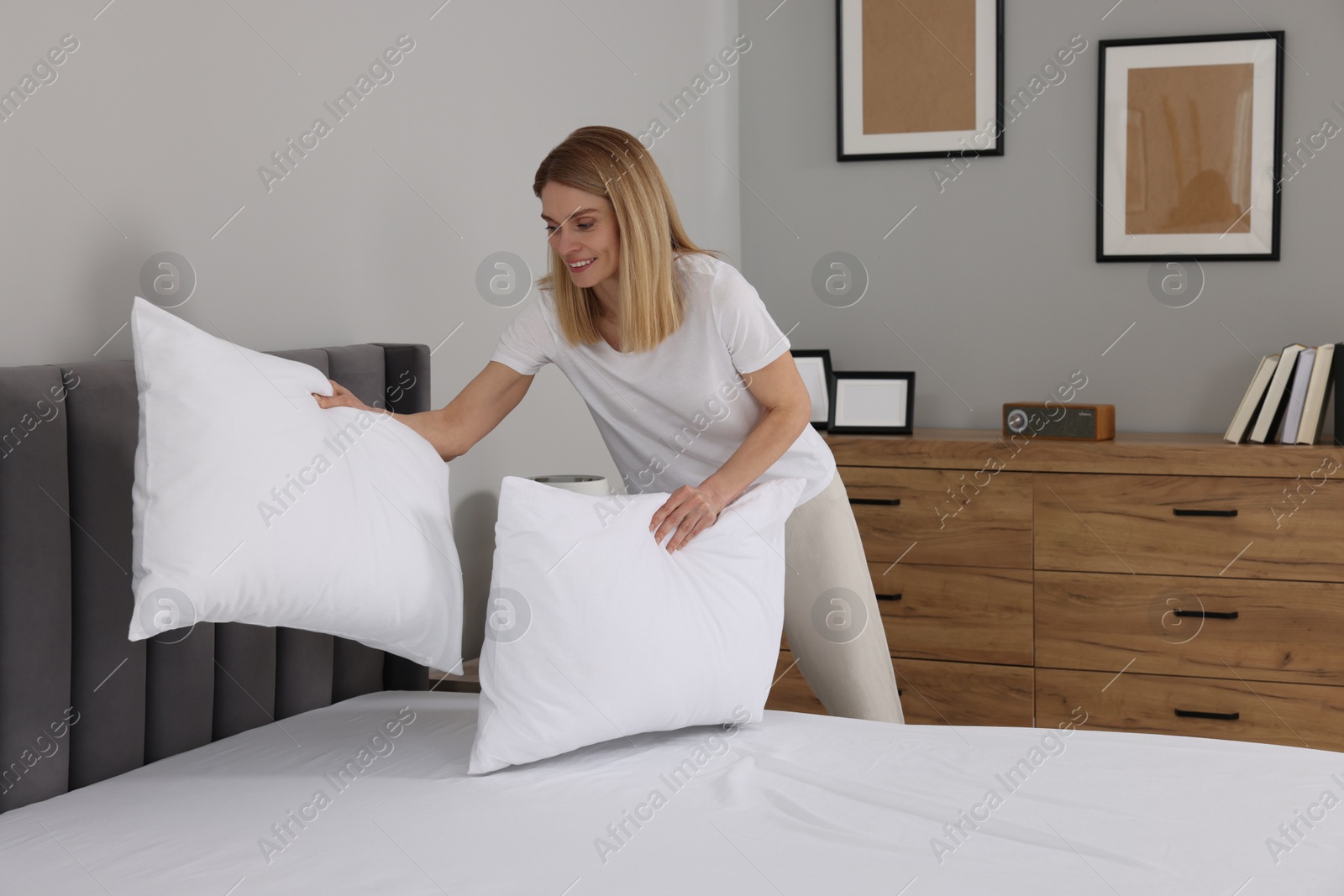 Photo of Woman putting pillows on bed at home. Space for text