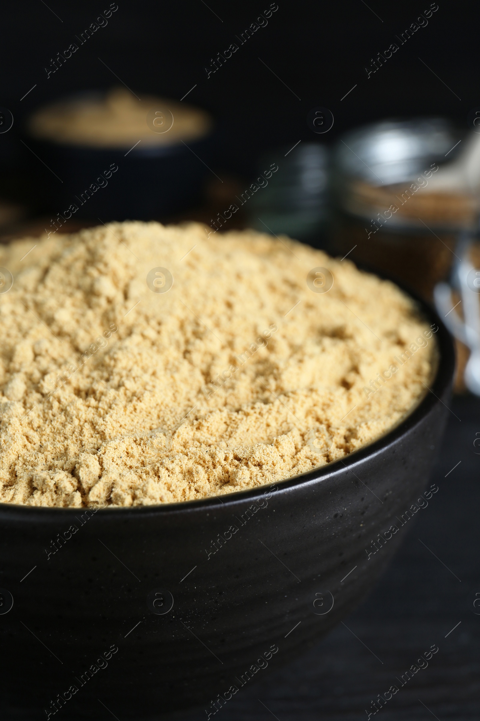 Photo of Bowl of aromatic mustard powder on black wooden table, closeup