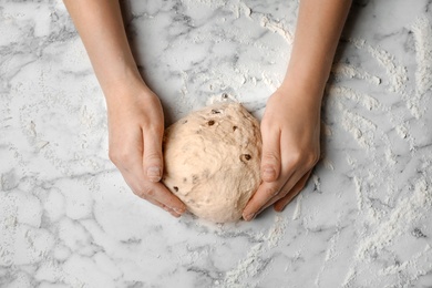 Photo of Young woman kneading dough at table, top view