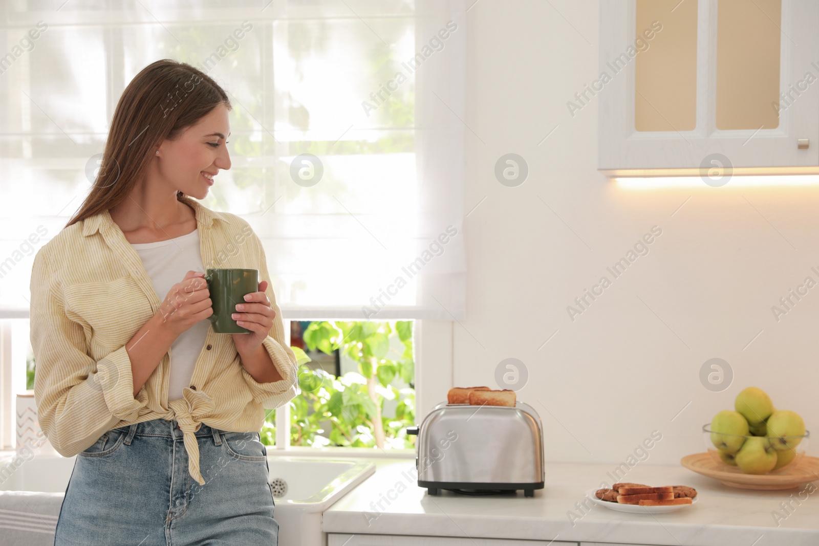 Photo of Young woman near toaster with slices of bread in kitchen