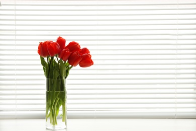 Photo of Window with blinds and beautiful bouquet on sill, space for text