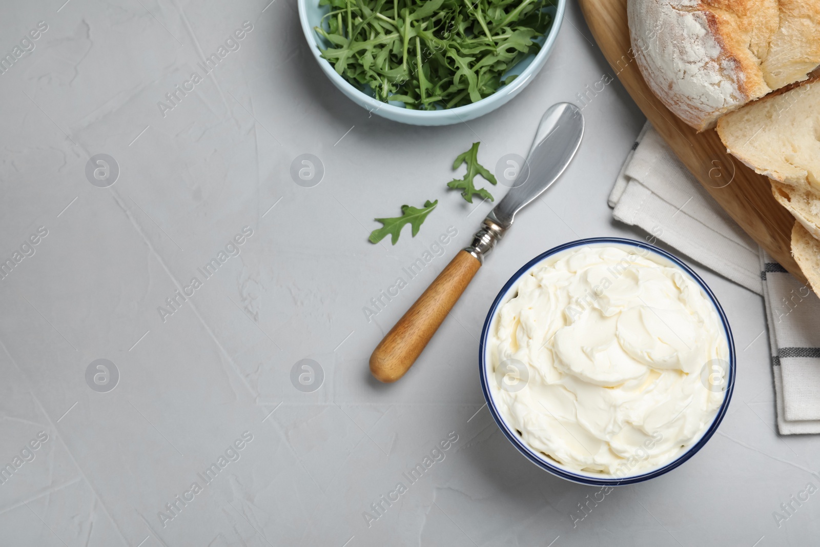 Photo of Tasty cream cheese, fresh bread and arugula on grey table, flat lay. Space for text