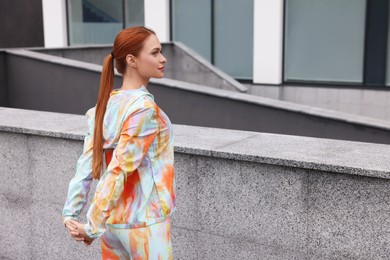 Beautiful woman in gym clothes doing exercises on street, space for text