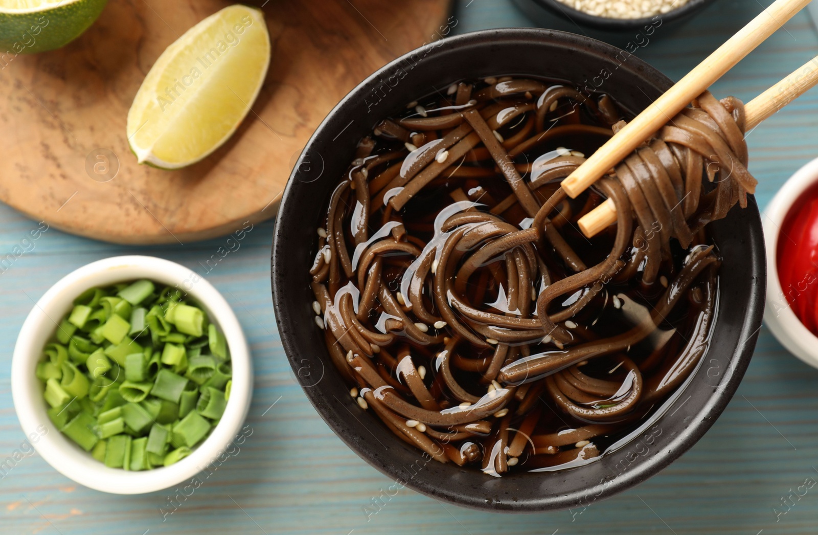 Photo of Eating delicious buckwheat noodle (soba) soup with chopsticks at light blue wooden table, top view