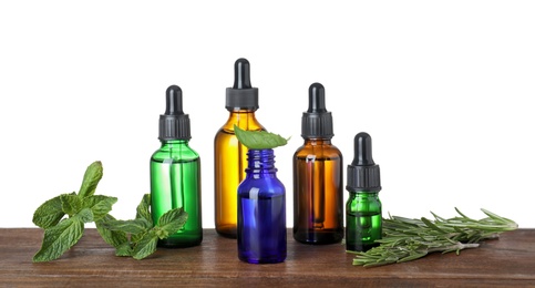 Photo of Bottles of herbal essential oils on wooden table against white background